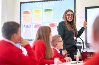 A female teacher standing at the front of a classroom with students looking at the whiteboard