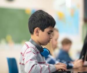 school child in grey long sleeved top sat at classroom desk