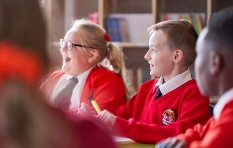 Four school pupils in red school uniform sitting at classroom table smiling