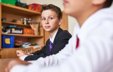 Secondary school student sitting in a classroom looking at his peer next to him