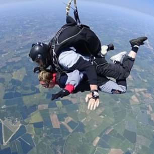 View from slightly above two people skydiving, with fields below